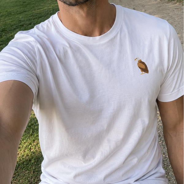 A man wearing a white t-shirt with a vulture embroidered on the left chest, photographed in a sunny park setting.
